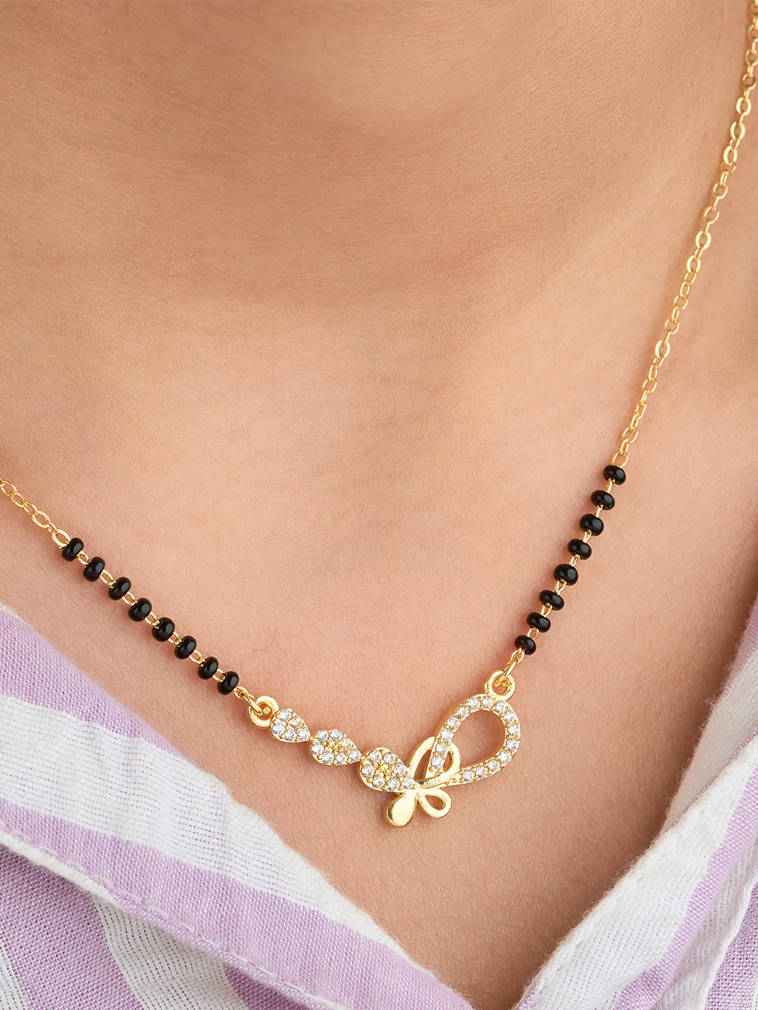 Gold necklace with black beads and a decorative clasp on a person wearing a light purple garment.