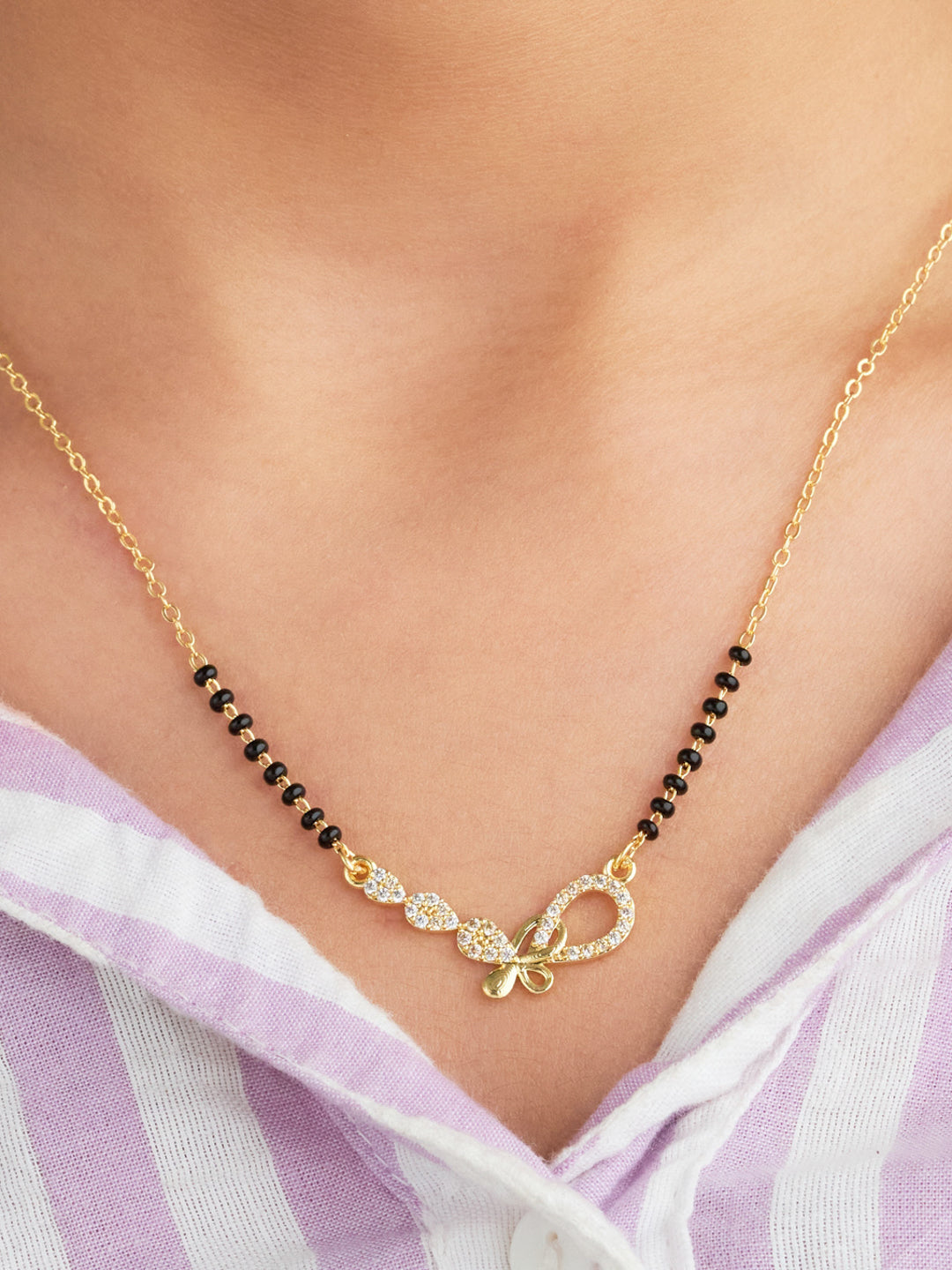 Gold necklace with black beads and a bow pendant on a person wearing a white and purple striped shirt.
