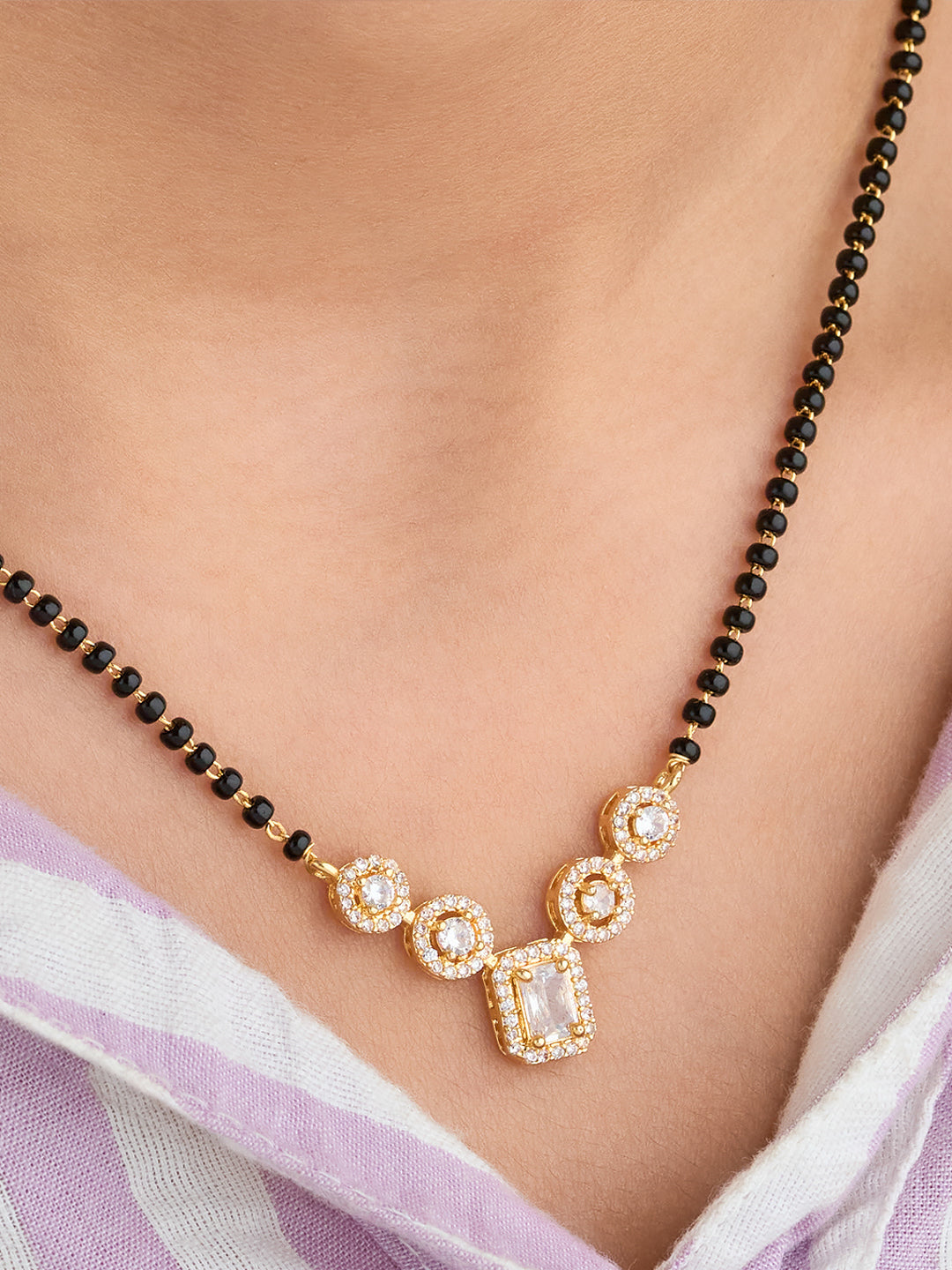 Necklace with black beads and gold and crystal pendant on a person wearing a light purple saree.