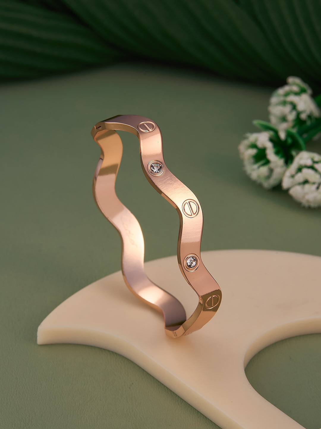 Rose gold bracelet with diamond accents on a beige stand against a green background