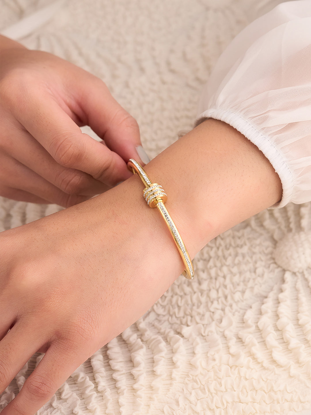 Gold bracelet being worn on a wrist with a textured beige background