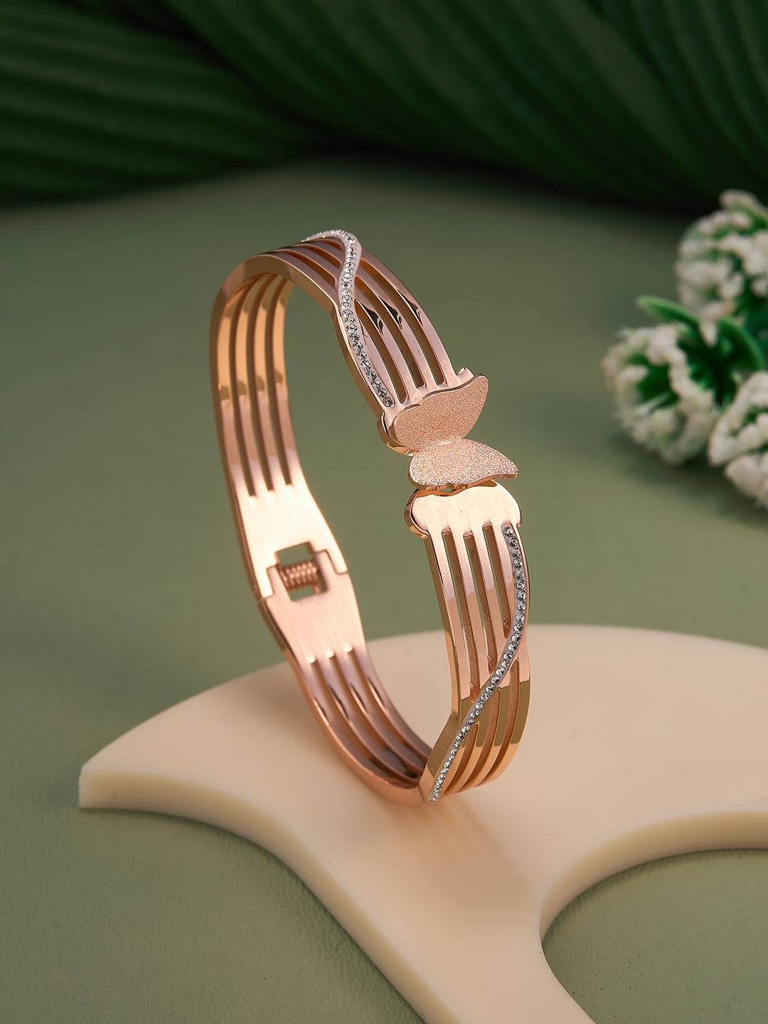Rose gold bracelet with a unique design on a beige stand against a green background