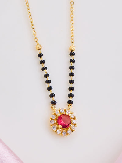 Necklace with black beads and a red gemstone pendant on a light pink background