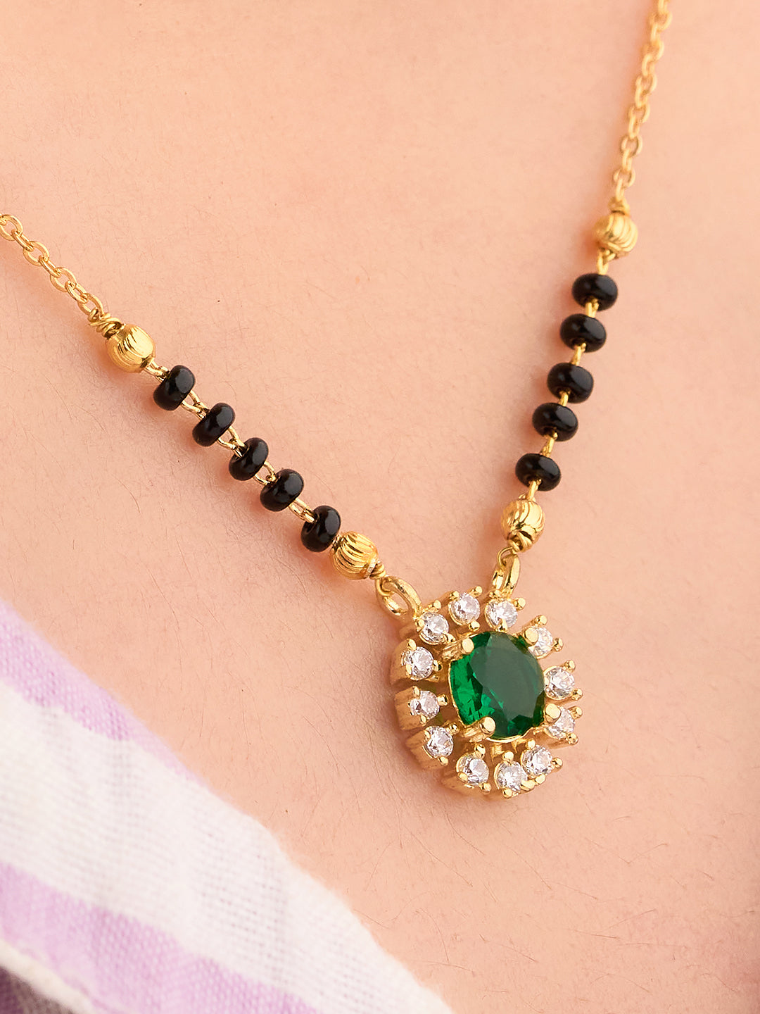 Gold necklace with green gemstone pendant on a person wearing a white and pink garment.
