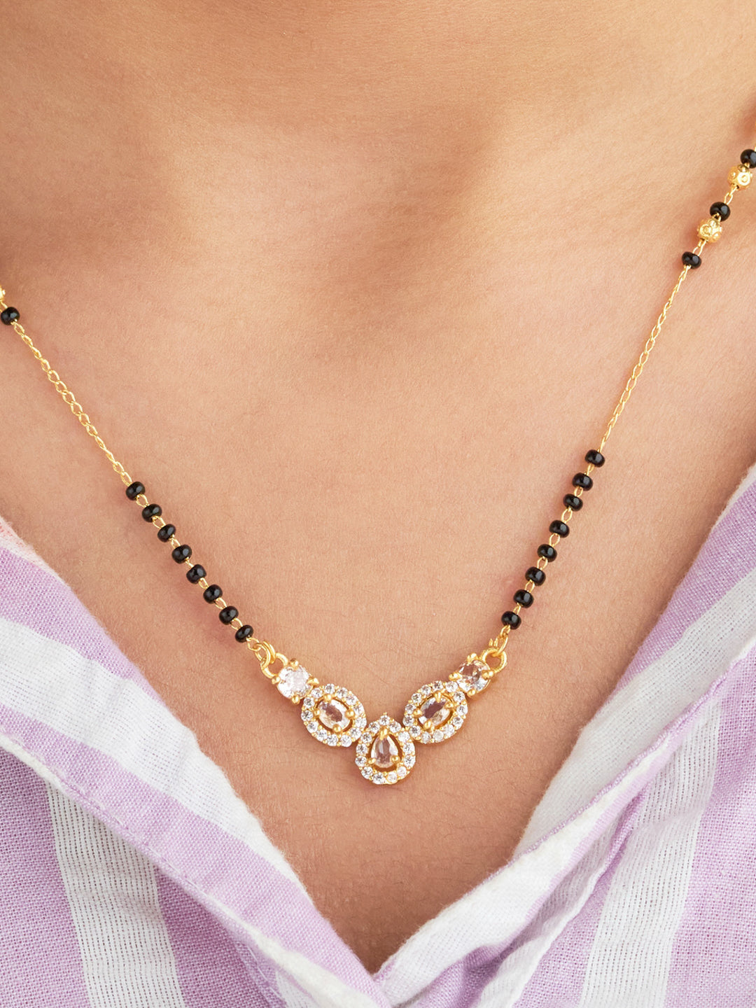 Gold necklace with black beads on a person wearing a light purple top.
