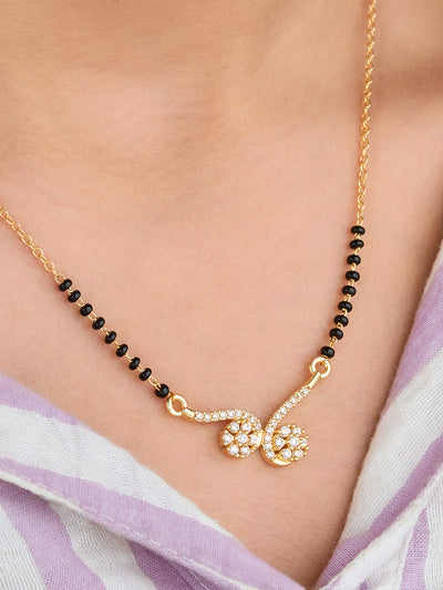 Gold necklace with black beads and a floral pendant on a person wearing a light purple scarf.