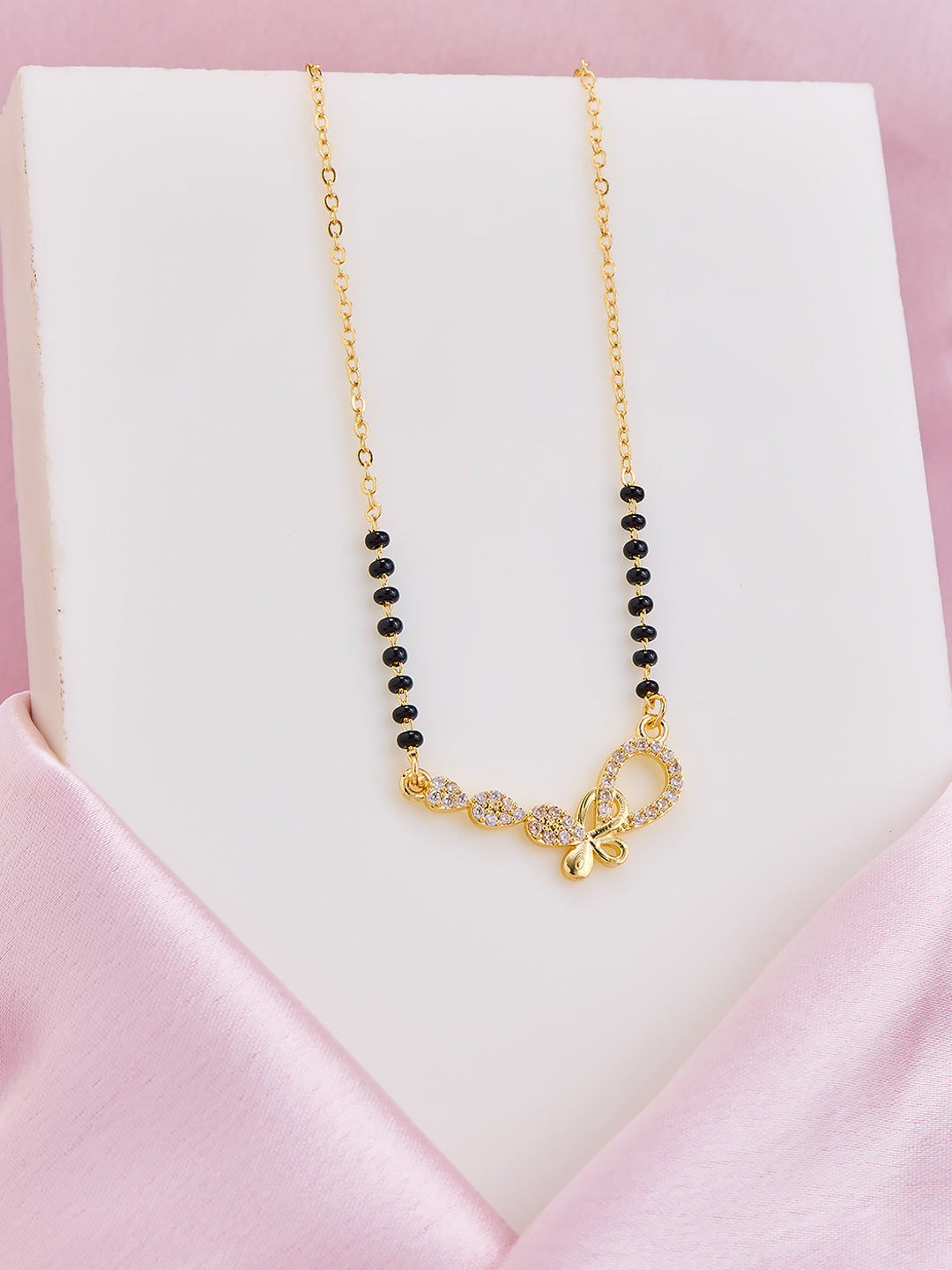 Gold necklace with black beads on a pink satin surface