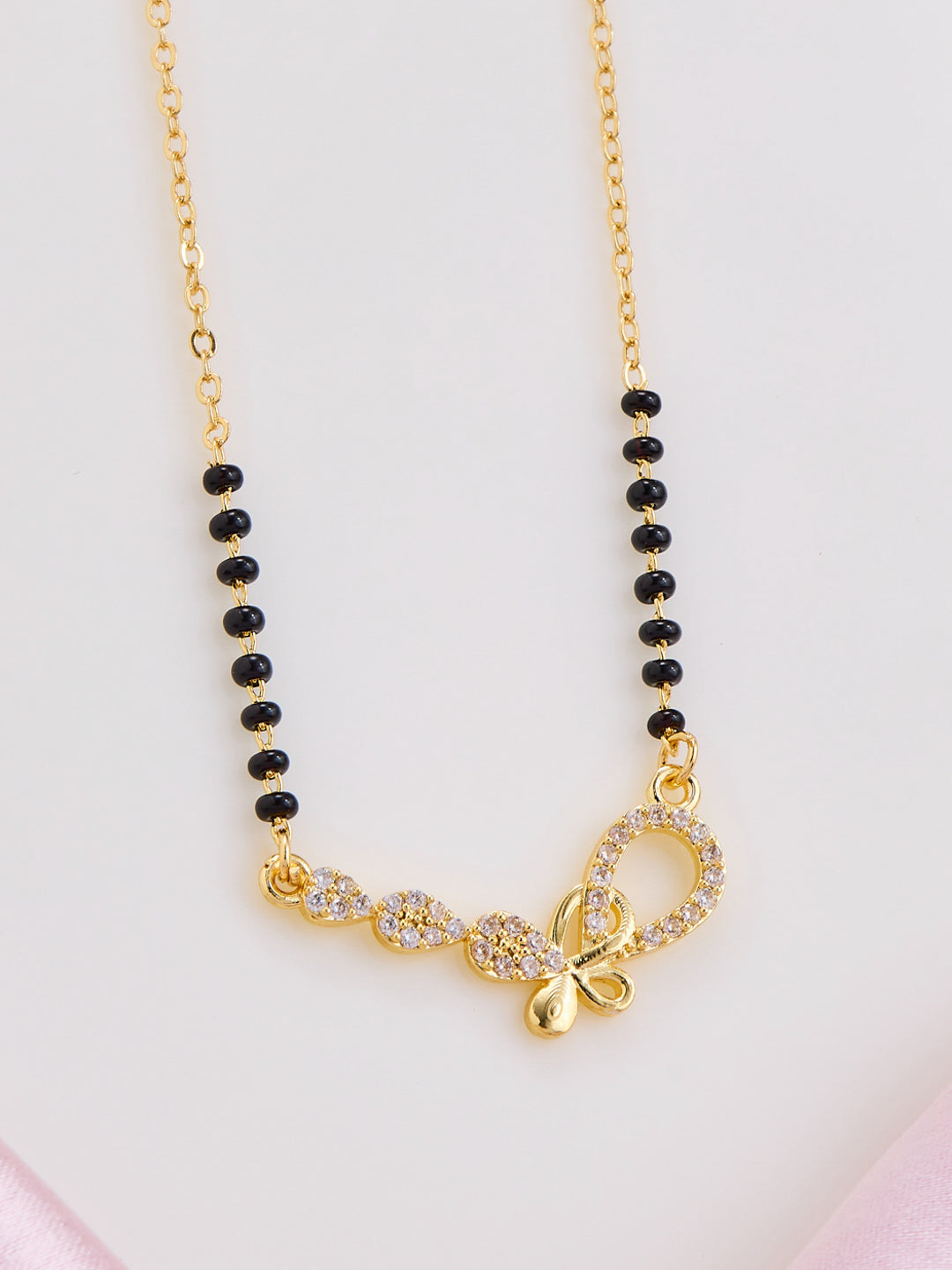 Necklace with gold chain, black beads, and butterfly pendant on a light pink background