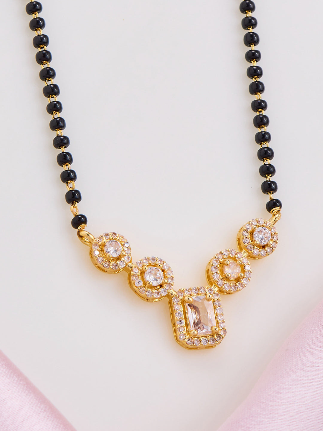 Necklace with black beads and gold and crystal pendant on a light pink background