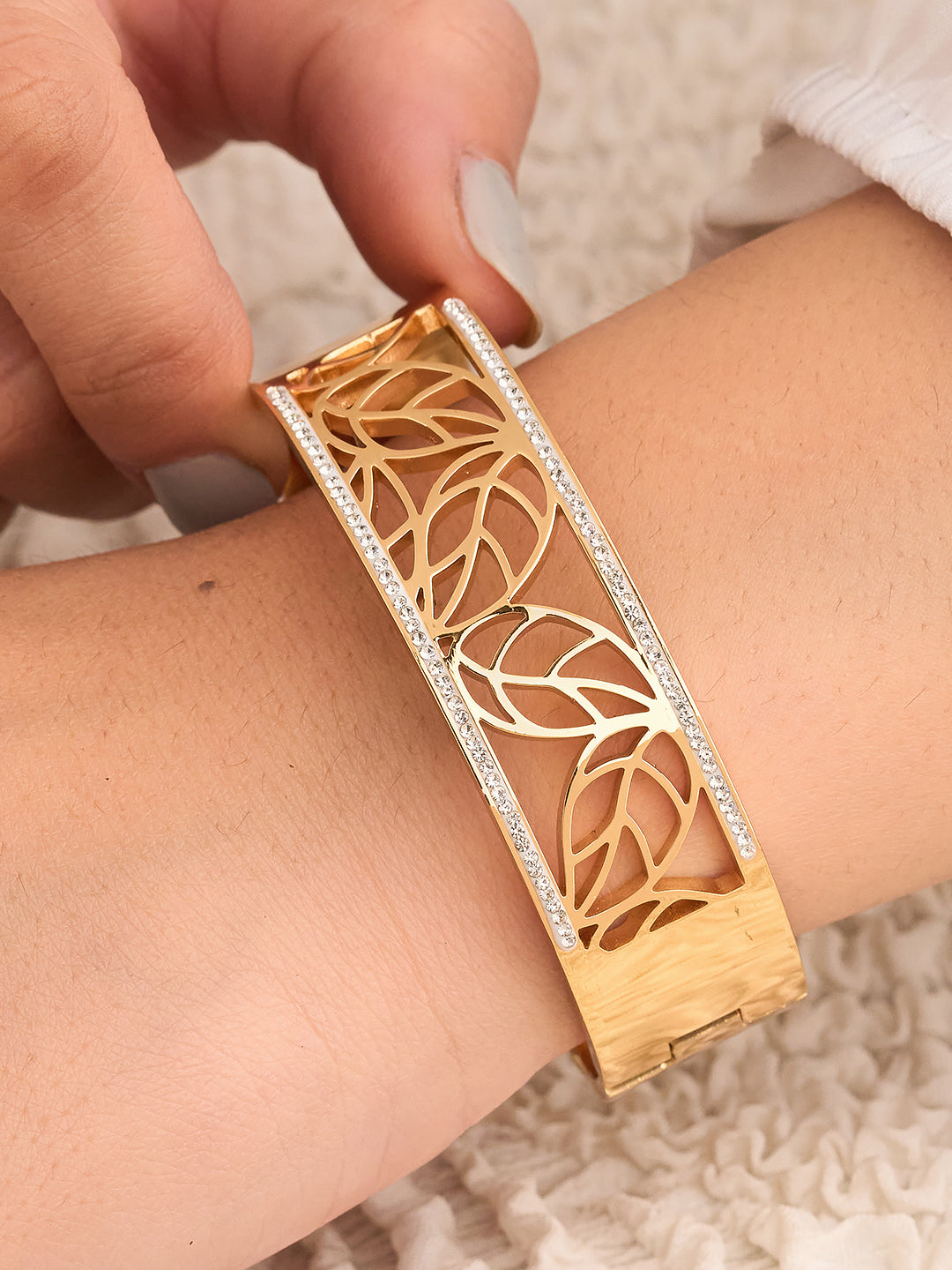 Gold bracelet with leaf design worn on a wrist against a neutral background