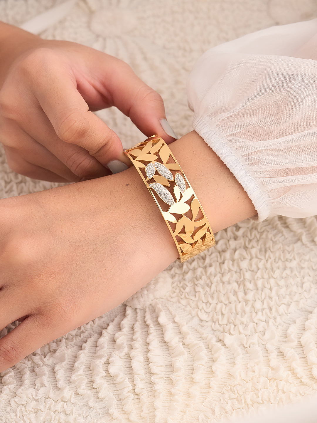 Gold bracelet with floral design worn on a wrist against a neutral background