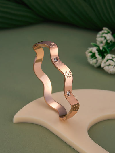 Rose gold bracelet with diamond accents on a beige stand against a green background