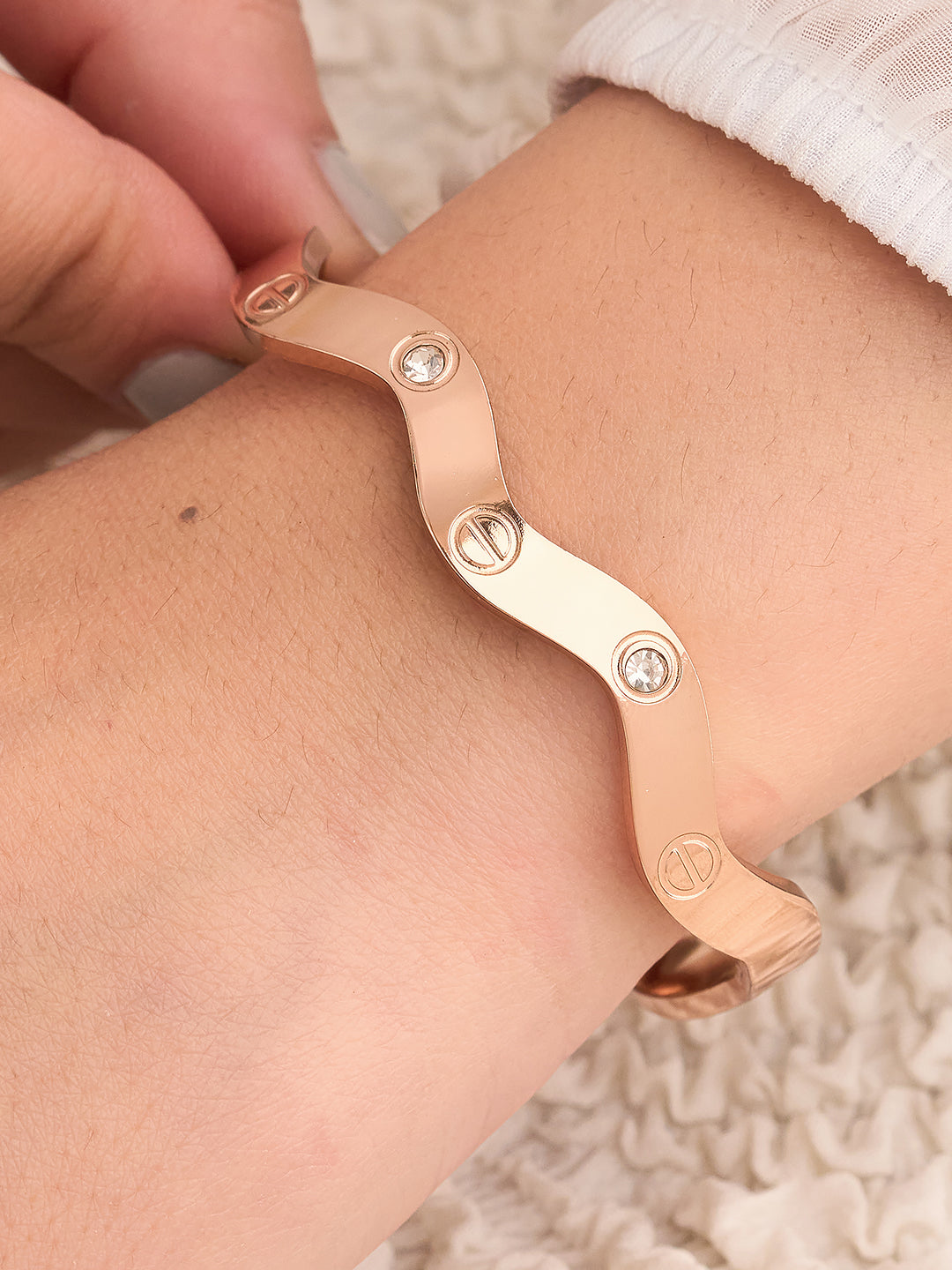 Rose gold bracelet with heart and circle designs worn on a wrist.