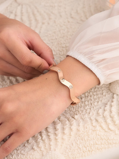 Person adjusting a gold bracelet on their wrist against a textured beige background