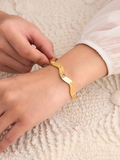 Gold bracelet being worn on a wrist with a neutral background