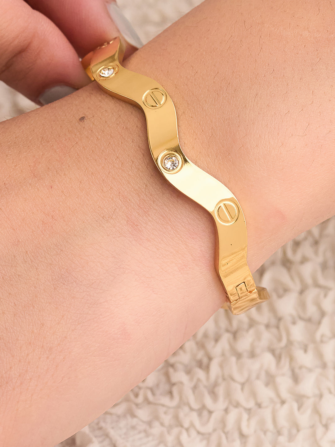Gold bracelet on a wrist with a neutral background