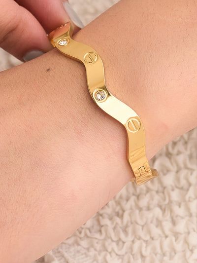 Gold bracelet on a wrist with a neutral background