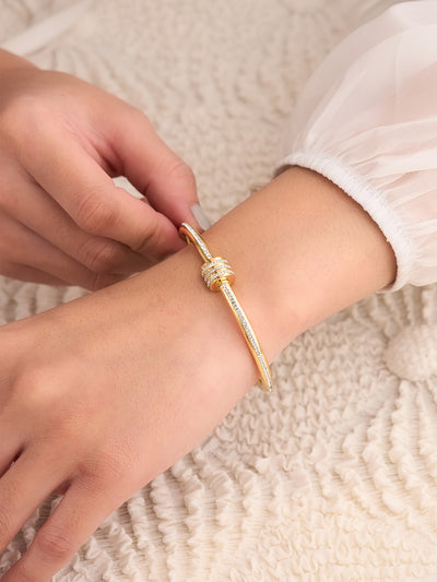 Gold bracelet being worn on a wrist with a textured beige background