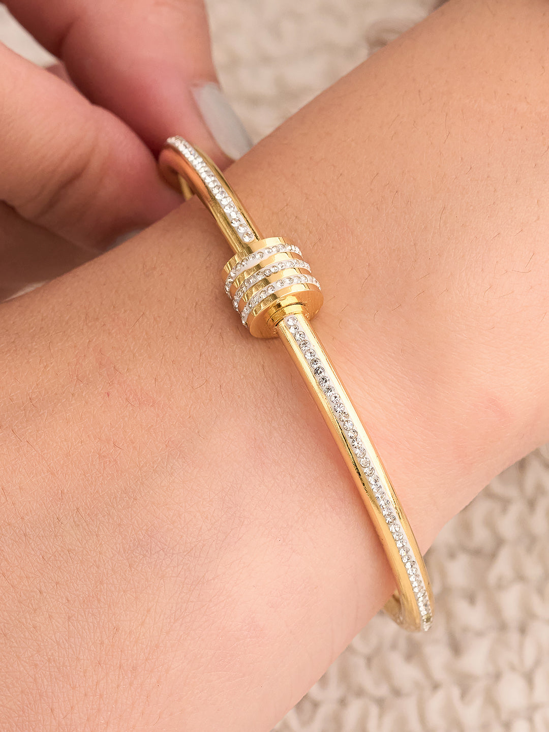Gold bracelet with diamond accents on a wrist against a neutral background